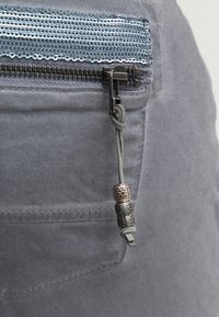 Šedá denimbavlna s kapsou na zip, která má modrý flitrový akcent. Na zipu je dekorační taháček se stříbrnými a bronzovými korálky.