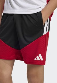 Red and black athletic shorts with a textured pattern, white accents, side pockets, and an Adidas logo on the lower left leg.