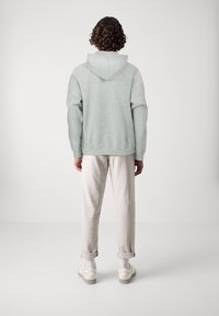 Lichtgrijze hoodie met een losse fit en geribbelde manchetten, gecombineerd met lichtbeige broeken en witte sneakers, gezien vanuit de achterkant.
