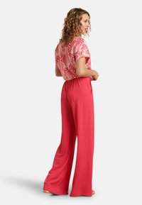 Pink wide-leg pants with textured fabric, paired with a short-sleeve blouse featuring a white wave pattern on a pink background.