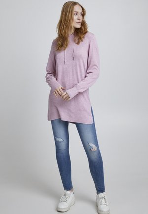 Ljusrosa hoodie i mjukt tyg, med dragsko, långa ärmar och sidofickor. Matchad med slitna blå skinnyjeans och vita sneakers.