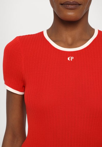 T-shirt rouge à côtes avec des manches courtes et un col rond blanc. Présente un petit logo au centre de la poitrine. Texture lisse.