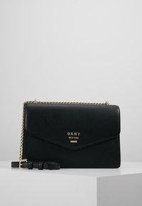 Svart läder axelremsväska med guldkedjearm, vikbar klaff och präglad logotyp på framsidan. Texturerad yta med minimala accenter.