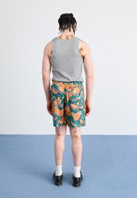Tricou fără mâneci gri, pantaloni scurți cu model abstract multicolor, șosete albe, pantofi negri, marcaje vizibile pe piele, fundal neutru.