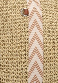 Geweven natuurlijk rieten tas met een beige en bruine chevronpatroon schouderband en bruine leren accenten, met een zilveren ring bevestiging.