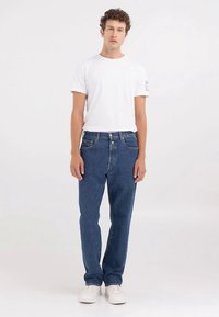 Mėlyni džinsai iš džinso audinio, tiesaus kirpimo, dėvimi su paprastu balta marškinėliai. Yra standartinės kišenės ir sagų uždarymas.