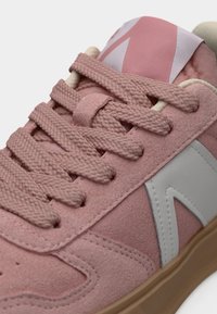 Baskets en daim rose avec des lacets tissés épais, logo latéral blanc et semelle en caoutchouc beige, gros plan sur le laçage et les détails du dessus.