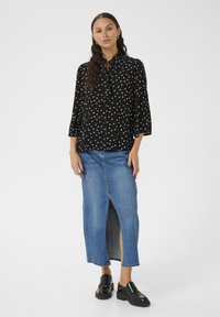 Black blouse with white polka dots, buttoned front, and 3/4 sleeves, paired with a blue denim maxi skirt featuring a front slit. Black loafers.