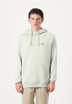 Light green hoodie featuring a front pocket, adjustable drawstring hood, and a small logo patch on the chest. Fabric has a smooth texture.