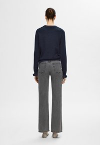 Mörkblå stickad tröja som kombineras med höga grå vida jeans. Jeansen har bakfickor och en lätt frans vid nederkanten.