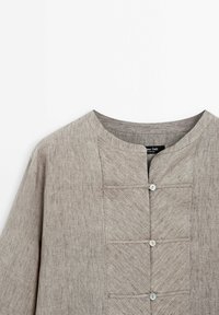 Grijze linnen shirt met een ronde halslijn, voorzien van een knopenlijst en drie horizontale zakken met een gestructureerde afwerking.