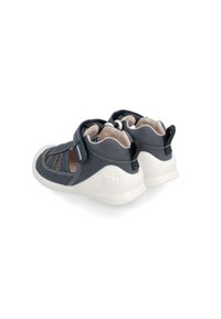 Dunkelblaue Stoffschuhe mit ausgeschnittenem Design, Klettverschluss und weißer Gummisohle. Verfügt über gestickte Akzente und ein Logo auf der Ferse.