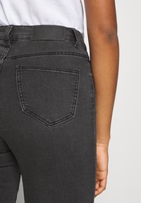 Jeans de mezclilla negra con un diseño ajustado, que cuentan con un único bolsillo trasero y un parche de cuero de la marca en la cintura. Textura suave.
