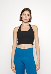 Top halter cropped preto combinado com leggings azuis de cintura alta. Tecido liso e elástico com um design ajustado, destacando a metade do abdómen.