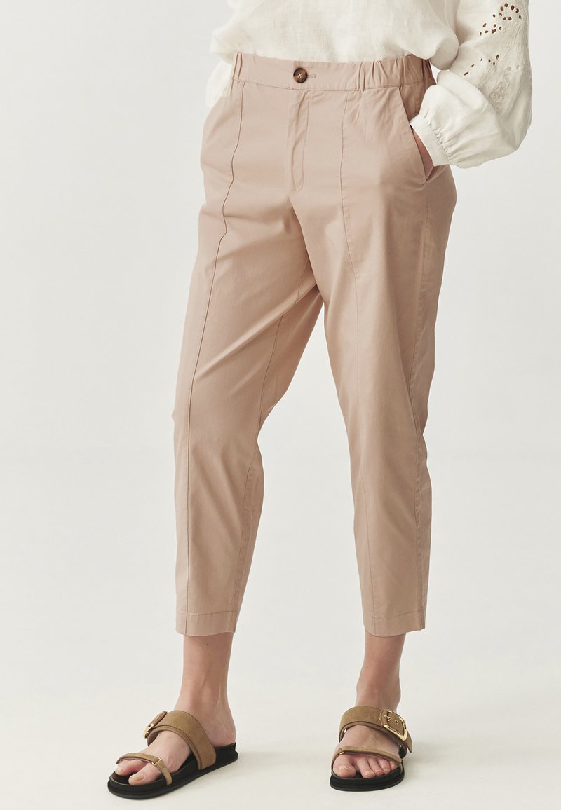 Light pink, belted cropped trousers with side pockets, a button closure, front pleats, and a smooth, lightweight fabric texture.