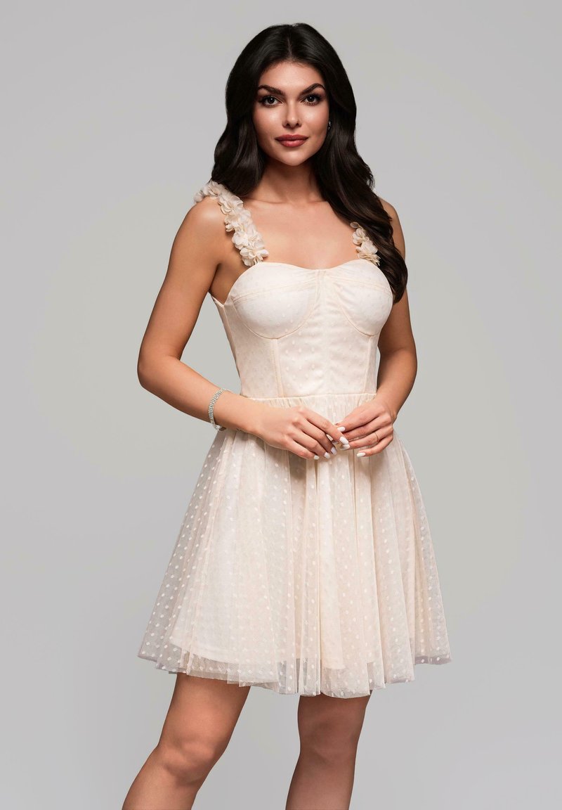 Das Kleid verfügt über einen taillierten Oberteil mit herzförmigem Ausschnitt, einem gepunkteten Muster, Rüschenbändern und einem ausgestellt Tüllrock in hellem Beige.