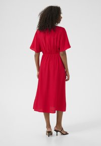 Red midi dress with a relaxed fit, short sleeves, elastic waistband, and flowing fabric. Worn with black heeled sandals.