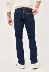 Dark blue denim jeans with a slim fit, featuring back pockets, contrasting stitching, and a tan leather accent on the waistband.
