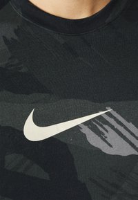 Svart träningströja med kamouflage-mönster, med en framträdande vit Nike-logotyp. Tyget ser strukturerat och lätt ut.