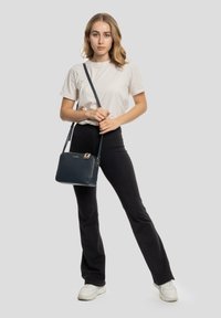 Borsa a tracolla navy con texture in pelle martellata, dettagli in zip dorate e una tracolla rimovibile, portata da una persona in abbigliamento casual.