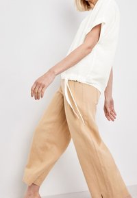 Haut en lin blanc avec un ourlet à cordon de serrage, associé à un pantalon large en lin beige. Les tissus semblent légers et texturés.