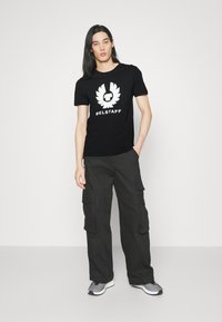 Svart bomull t-shirt med en vit logotyp och text. Kombinerad med lösa svarta cargo-byxor med sidofickor. Grå sportskor.