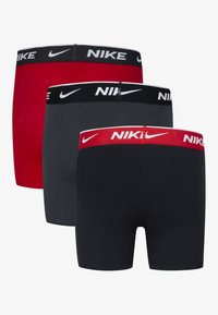 Trije pari moških Nike bokser hlačk: rdeče, sive in temno modre barve. Vsak ima elastičen pas z blagovno znamko in belim logotipom. Mehka tkanina iz bombažne mešanice.