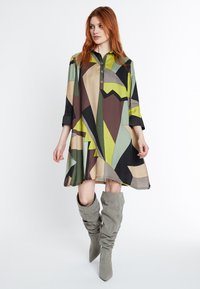 Buntes, kragenloses Kleid mit einem geometrischen Muster in Grün, Braun und Beige. Aus leichtem Stoff mit Dreiviertelärmeln gefertigt.