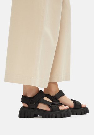 Czarne platformowe sandały z regulowanymi paskami wykonane z materiału syntetycznego, z grubą teksturowaną podeszwą i odkrytymi palcami.