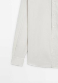 Chemise blanche à manches longues avec boutons et poignets visibles sur un fond blanc uni.