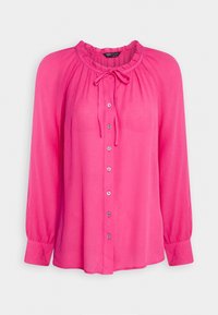 Blusa lunga rosa a maniche lunghe con scollatura rotonda, dettaglio con fiocco e chiusura a bottoni. Realizzata in tessuto leggero con una texture pieghettata.