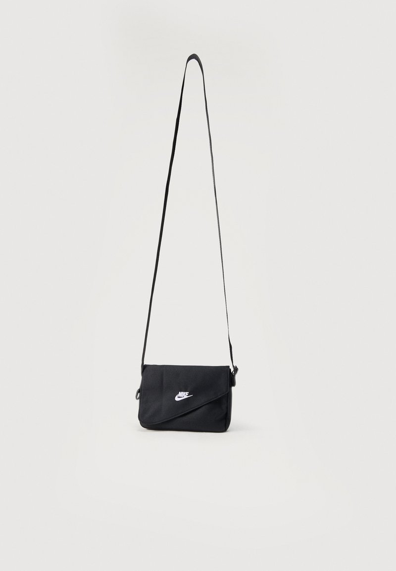 Čierna crossbody taška Nike s nastaviteľným popruhom a bielym logom na prednej klapke, zobrazená na jednoduchom svetlom pozadí.
