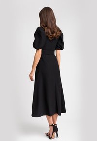 Czarna midi sukienka z bufiastymi rękawami, dopasowanym górą i rozkloszowanym dołem. Gładki materiał, zaznaczona talia i boczne rozcięcie. Noszona z czarnymi szpilkami.
