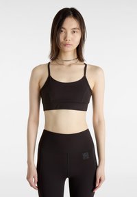 Schwarzer Sport-BH mit dünnen Trägern, glatter Textur und kontrastierenden Nähdetails. Kombiniert mit hochgeschnittenen schwarzen Leggings mit Logo.