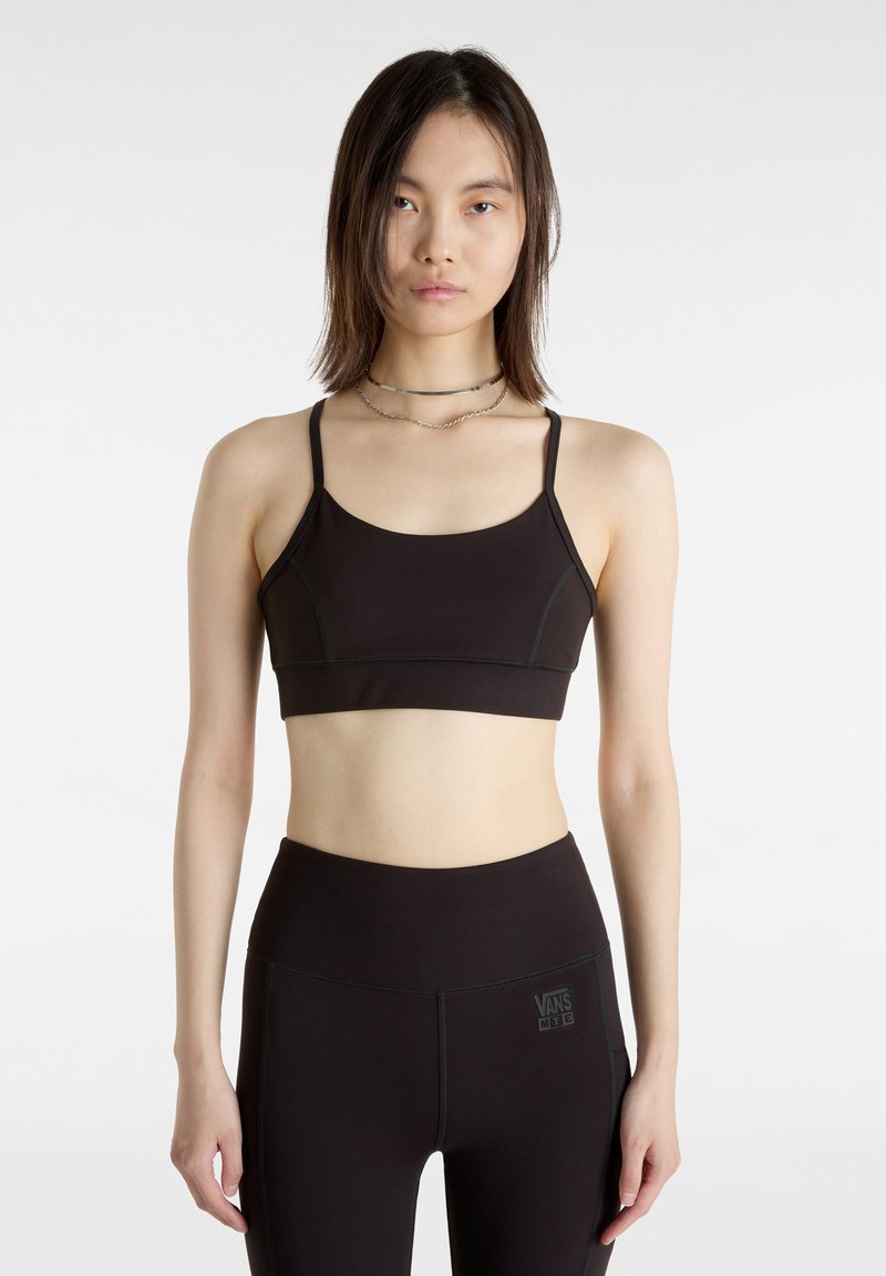 Zwarte sportbeha met dunne banden, een gladde textuur en contrasterende stikselafwerking. Draagt met high-waisted zwarte leggings met logo.