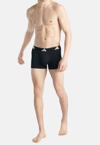Boxers noirs en tissu lisse, présentant une large taille avec des accents de logo Adidas blancs et une coupe ajustée.