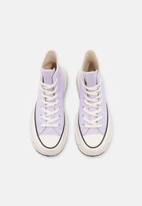 Höga sneakers i ljuslila canvas med cremefärgade snören, vit gummitåänd och texturerad sula. Anmärkningsvärd sömdetalj längs kanterna.