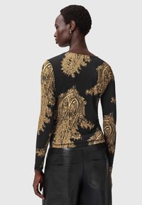 Must mustikasvargiga pikkade varrukatega tipp, millel on keerukad kuldsed paisley mustrid. Pehme kangas, eriti keha lähedane disain ja ümar kaelus.