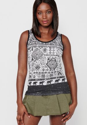 Schwarz-weiß gemustertes Tanktop mit tribal- und elefantischem Design, kombiniert mit einem grünen plissierten Rock.