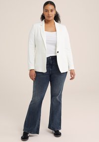 Bílý blazer s klopami a zapínáním na jeden knoflík, kombinovaný s tmavě modrými rozšířenými džíny a černými teniskami. Hladká textura látky.