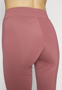 Leggings de couleur framboise avec un tissu lisse et extensible. Dotés d'une taille haute et d'un design ajusté, mettant en valeur une silhouette élégante.