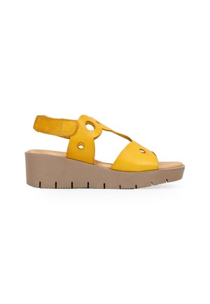 Sandalias de cuña de cuero amarillo con diseños troquelados, correa ajustable y una suela beige texturizada con detalles muescados.