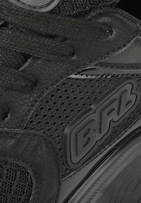 Baskets noires présentant une tige en cuir texturé, des panneaux en mesh et une semelle en caoutchouc. Logo de marque distinctif embossé sur le côté. Lacets noirs.