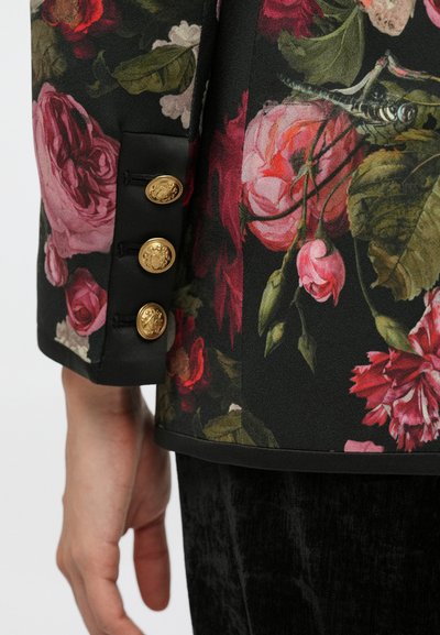 Fekete virágmintás blézer rózsaszín és piros rózsamintákkal, selyemszerű textúrával és három arany gomb díszítéssel az ujjatlanon.