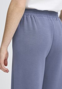 Pantalons en tissu doux de couleur violet clair avec une large ceinture. Texture lisse, design à jambes larges, ajustés à la taille. Pas de motifs ou d'accents visibles.