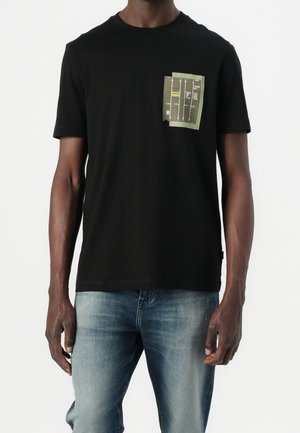 T-shirt en coton noir à manches courtes avec une poche avant ornée d'un motif graphique en vert et jaune. Texture lisse, coupe décontractée.