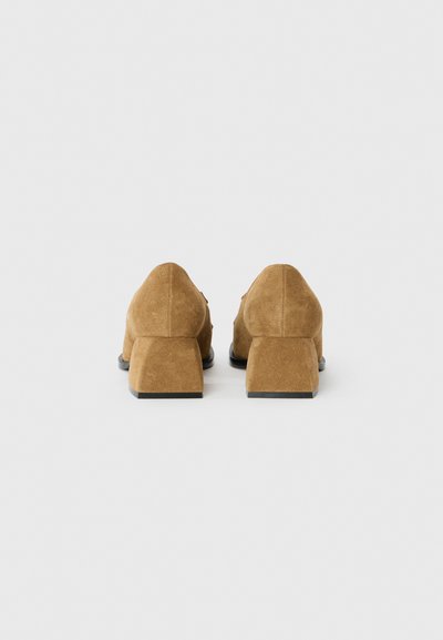 Chaussures en suède marron à talons carrés, avec une texture lisse et une forme angulaire, dotées d'un talon bas et empilé et d'un profil arrière pointu.
