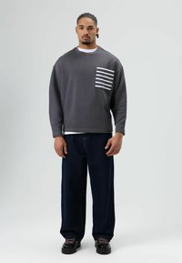 Gray sweatshirt with a striped pocket, paired with loose-fitting dark jeans. Black chunky shoes with pink laces complete the look.