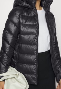 Svart pufferjacka med huva, som har dragkedja fram och horisontellt kviltat mönster. Slät, glänsande textur med en modern passform.