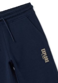 Pantalon de survêtement bleu marine en tissu doux, avec une taille élastique, des poches latérales et un logo imprimé "EXPLORE" en doré sur une jambe.